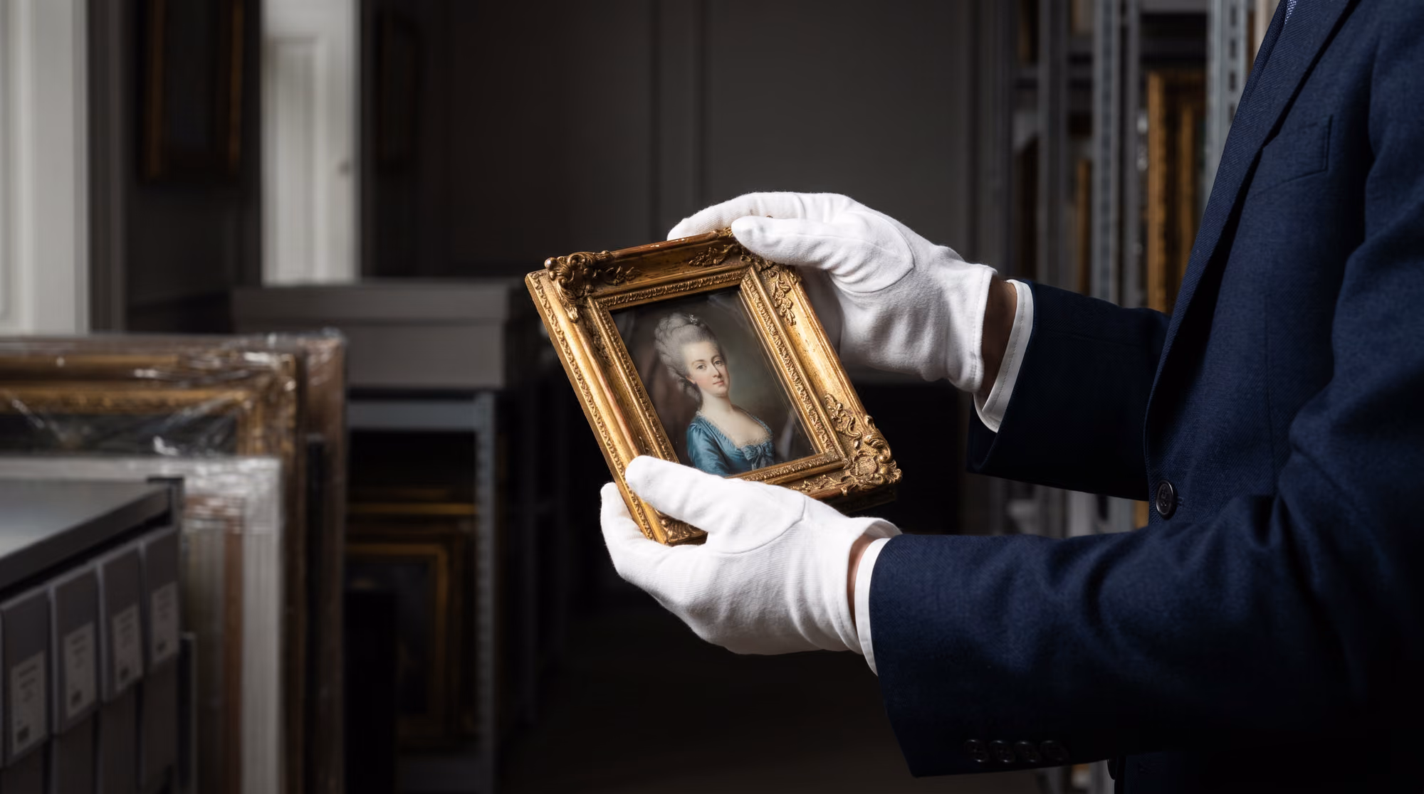 A gloved art handler holding a small framed portrait