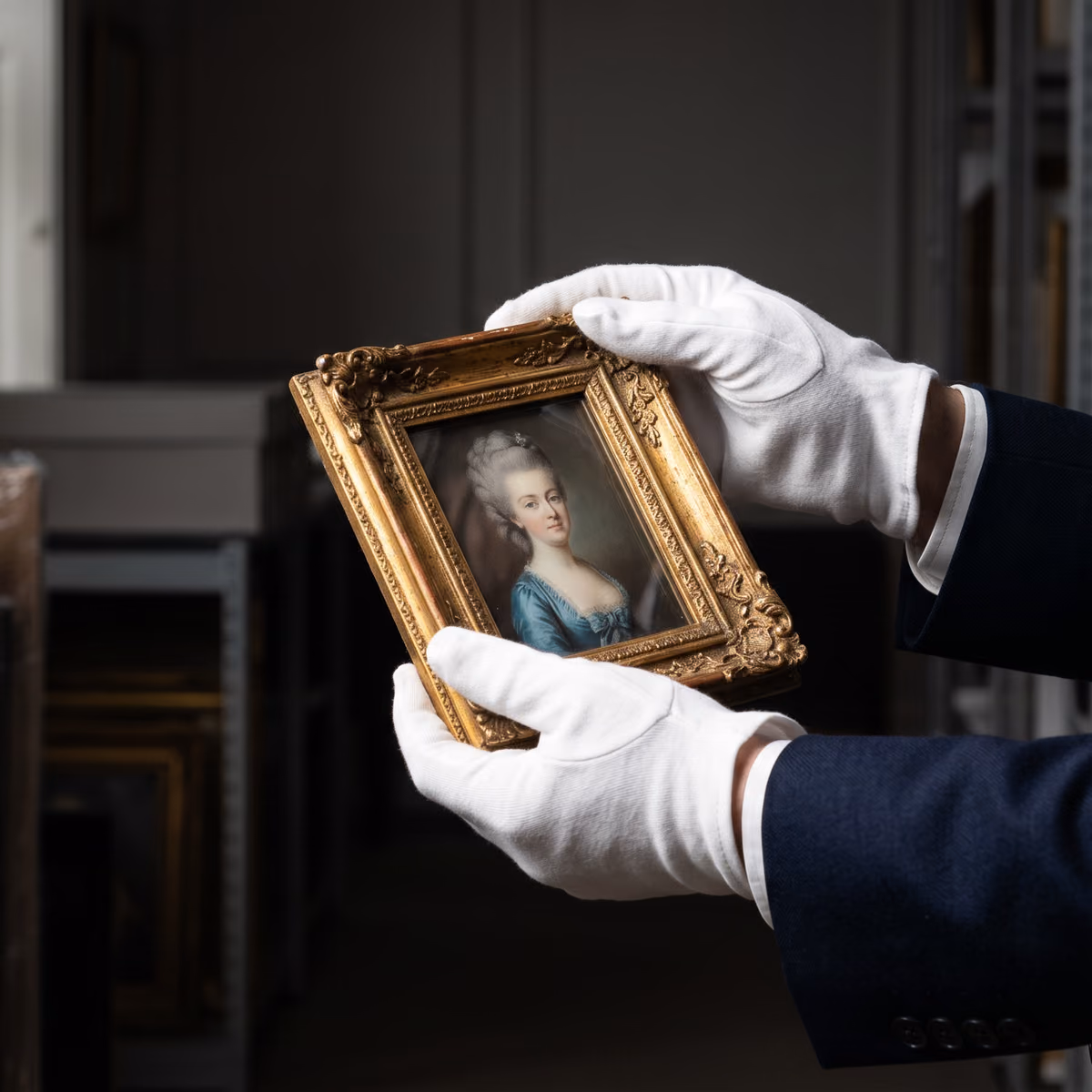 Gloved hands carefully holding a gilded framed portrait
