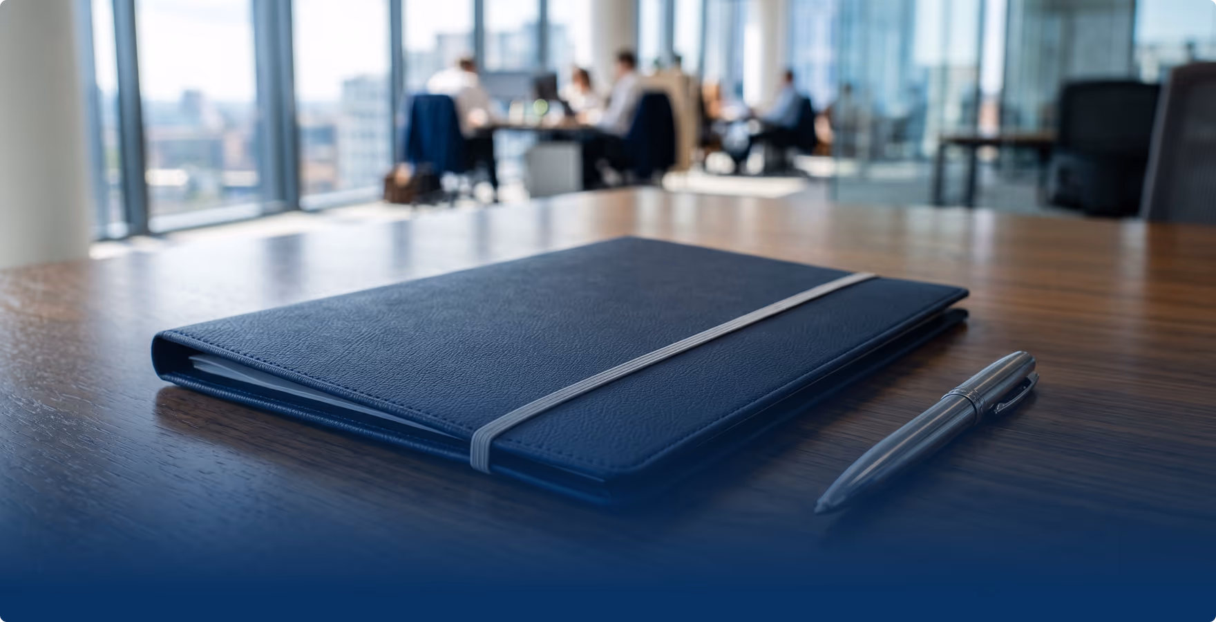 A leather notebook and pen on a desk in a modern office