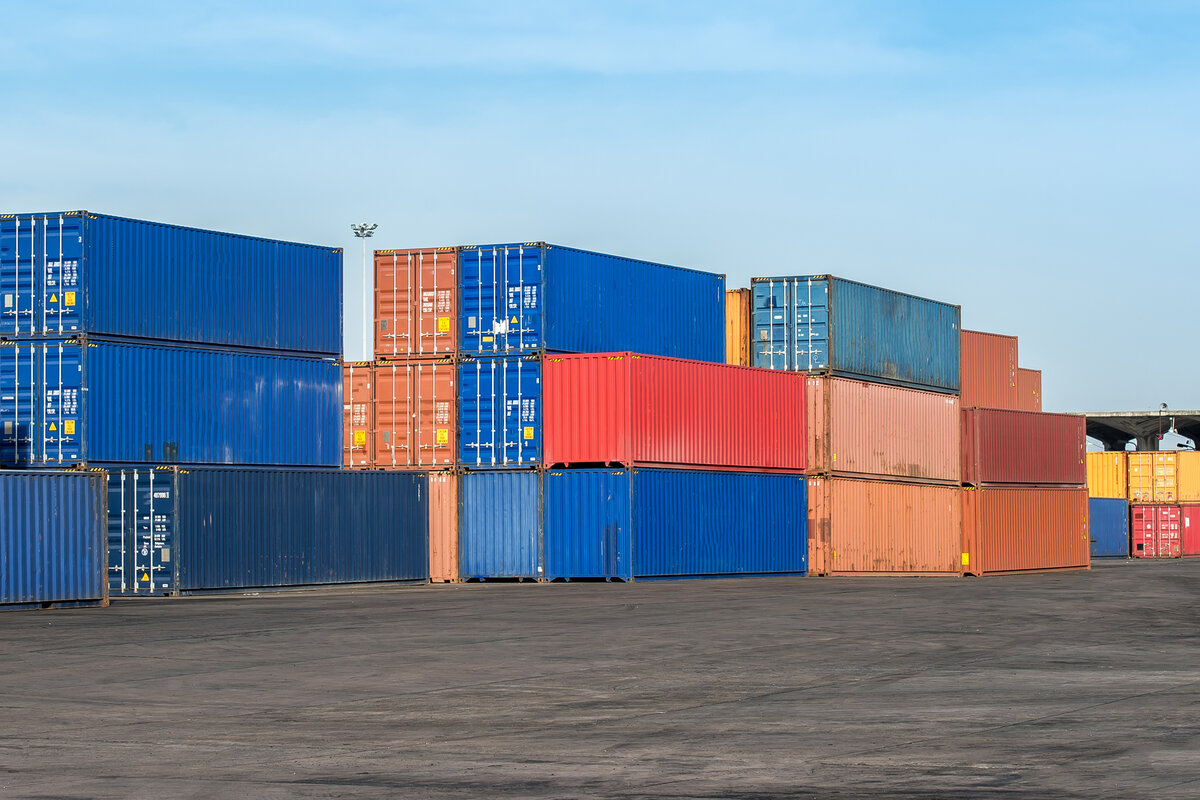 Stacked blue, red, and orange shipping containers in an industrial yard.