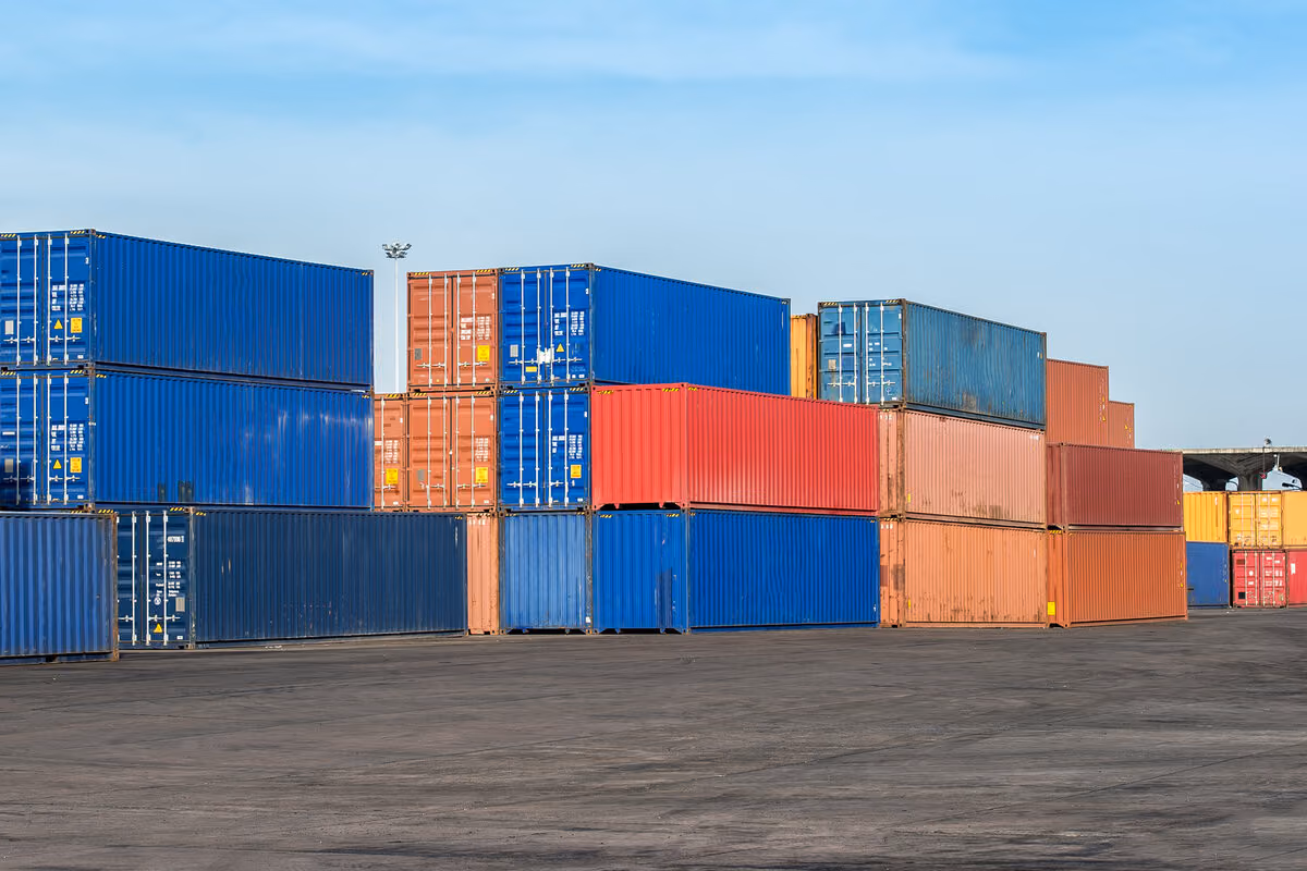Stacked blue, red, and orange shipping containers in an industrial yard.