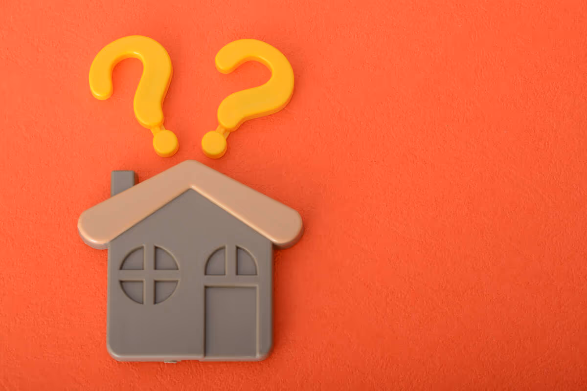 Gray house with two yellow question marks on orange, showing housing uncertainty.